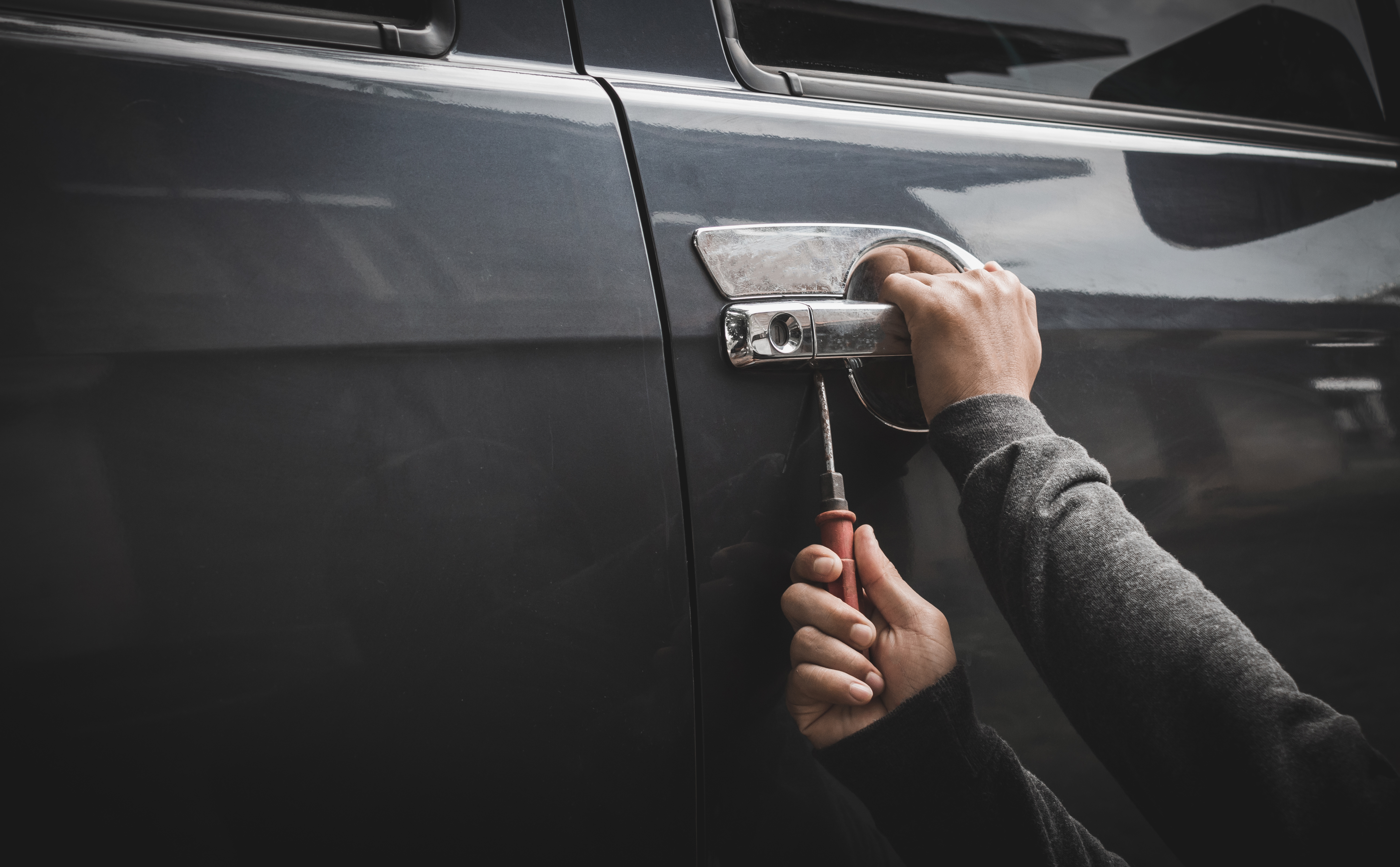 Man breaking into gray car with screwdriver