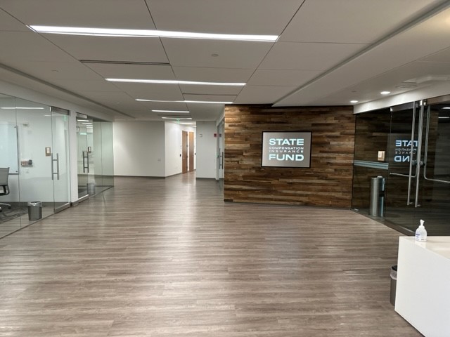Entrance to the State Fund Learning Center. Glass doors leading to meeting rooms on the left. Wooden wall with a State Compensation Insurance Fund sign.