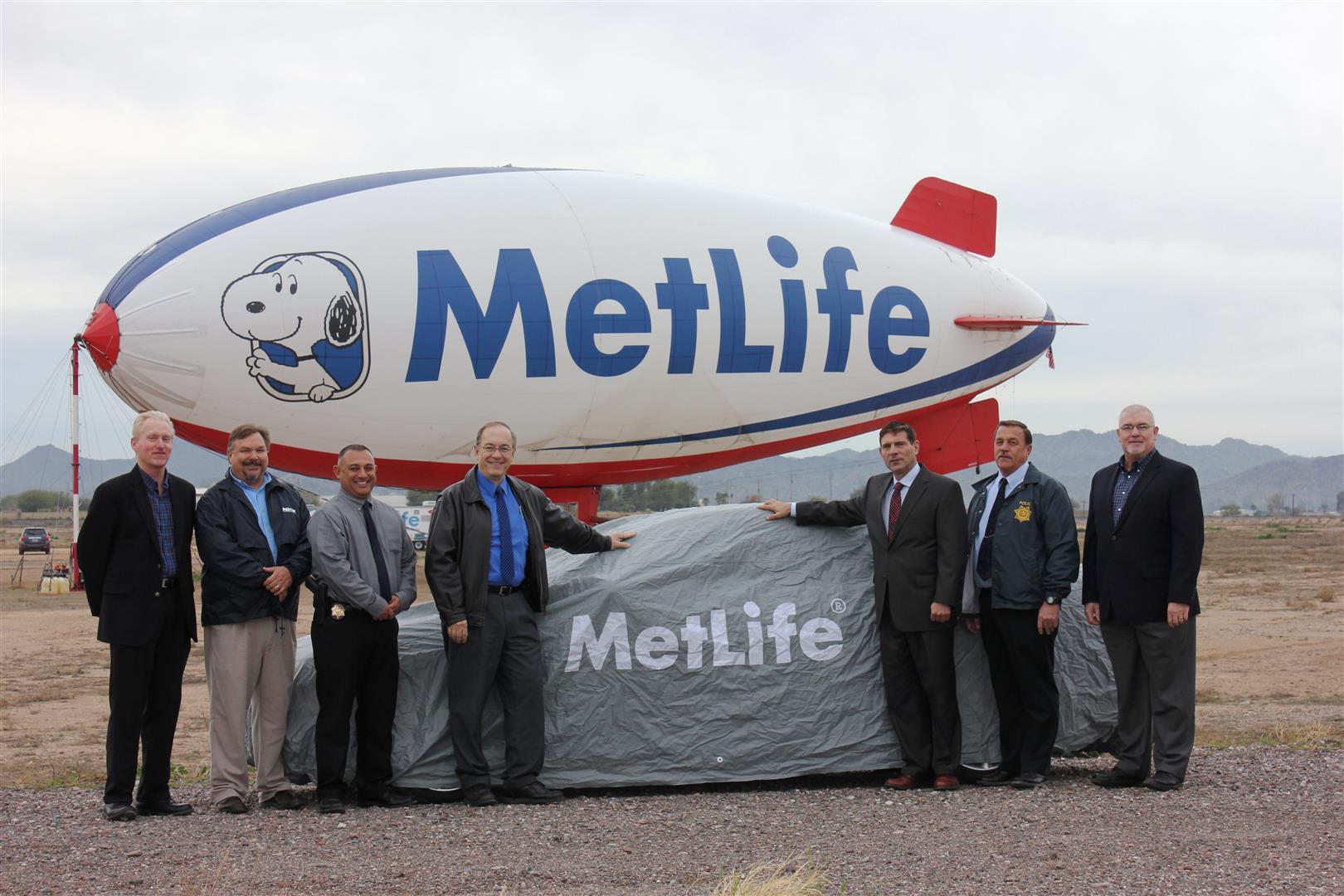 Men smiling in front of a covered vehicle with a MetLife blimp behind them
