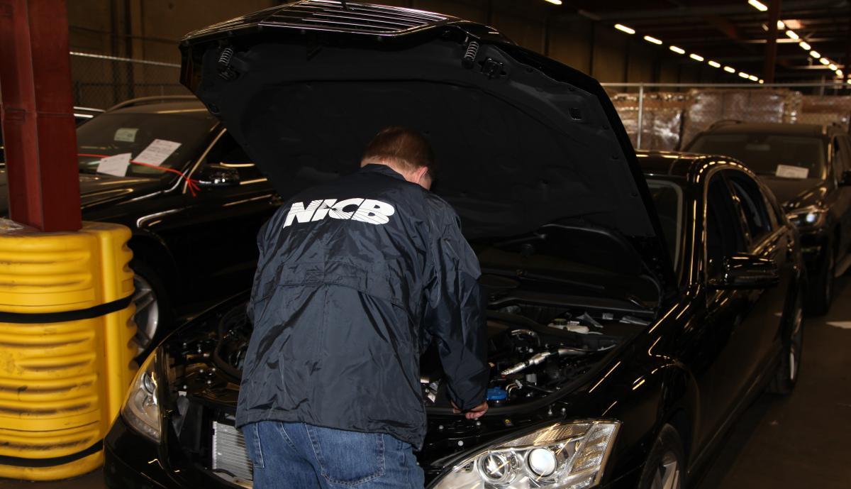 Man looking under the hood of a black vehicle.
